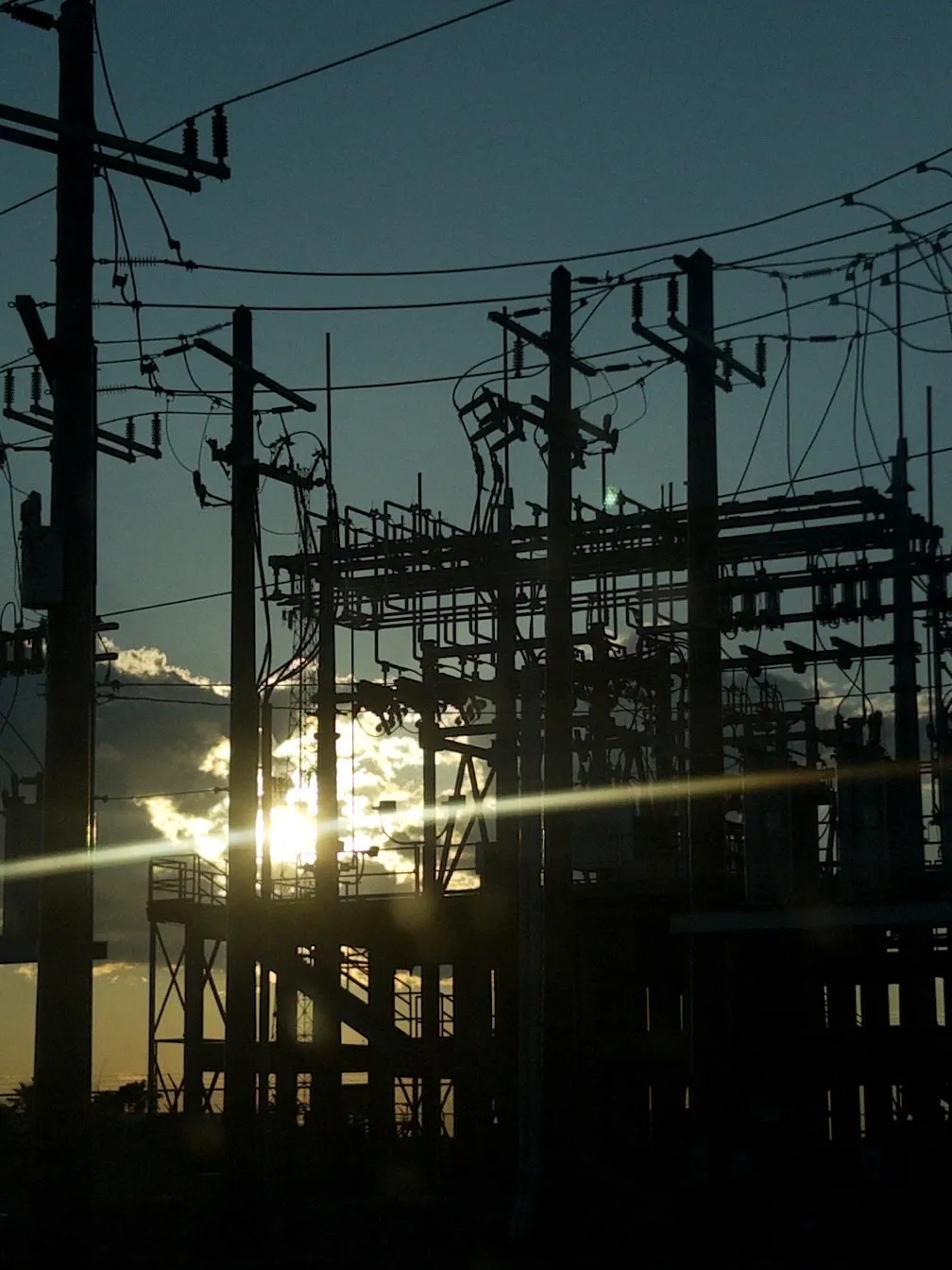 The sun cuts through the dark shadows of the power station poles and wires