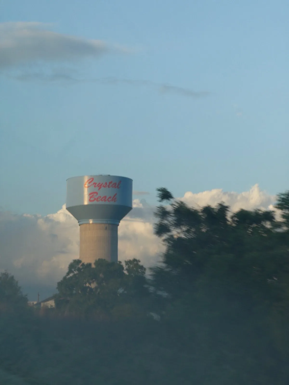 A water tower that reads "Crystal Beach" is seen in the distance, behind some trees