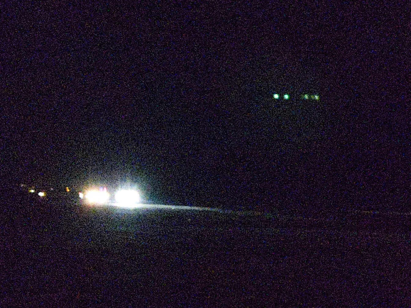 Car headlights bleed into the darkness, casting light on the sand